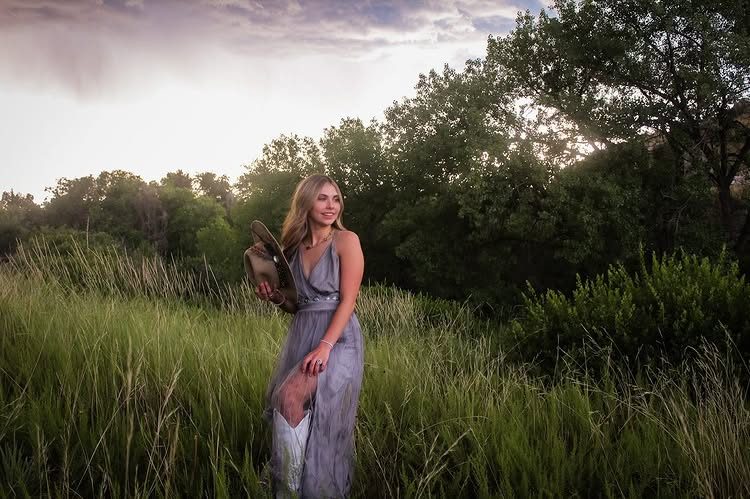 Kaylie Michelle holding a cowboy hat in a grassy field under a stormy sky