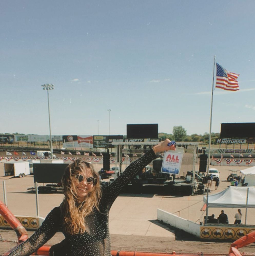 Kaylie Michelle smiling and holding up an all-access pass at an outdoor music event